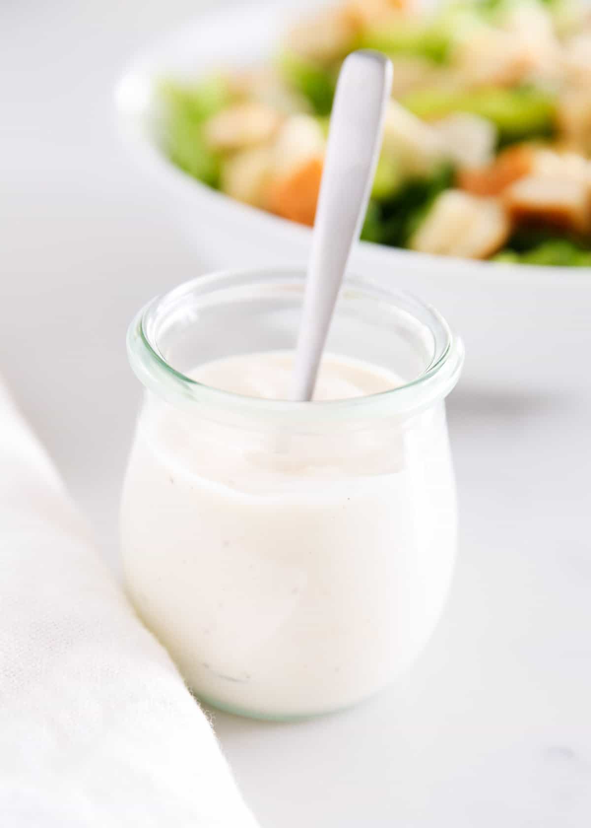 Caesar salad dressing in a glass jar with a spoon.