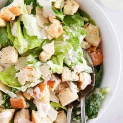 Caesar salad in a white bowl with croutons and parmesan.