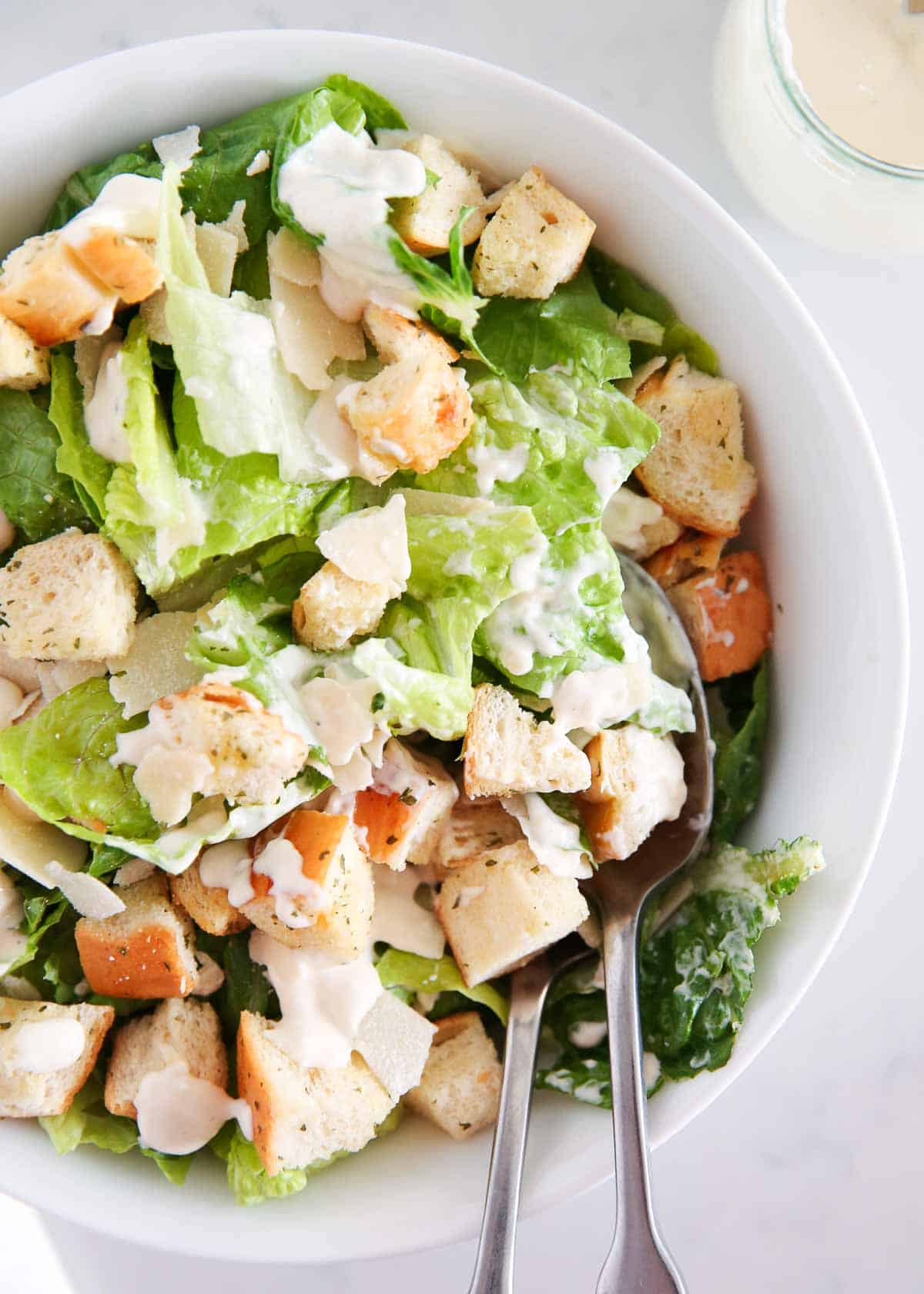 Caesar salad in a white bowl with croutons and parmesan.