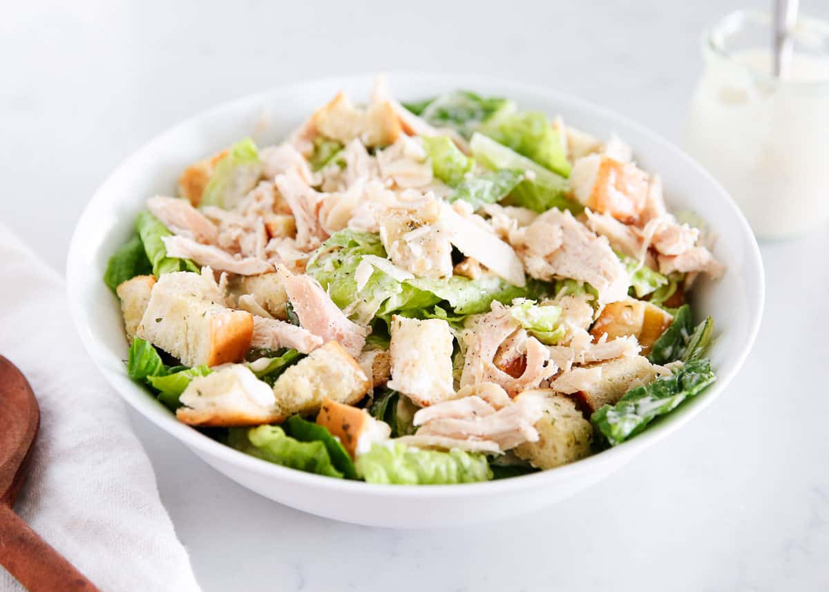 Ramp up the protein in your traditional caesar salad by adding flavorful chunks of chicken and turning it into chicken caesar salad for a quick and easy lunch or light dinner. Level it up with homemade croutons, a creamy homemade dressing, and shaved Parmigiano! Caesar salad with chicken in a white bowl.