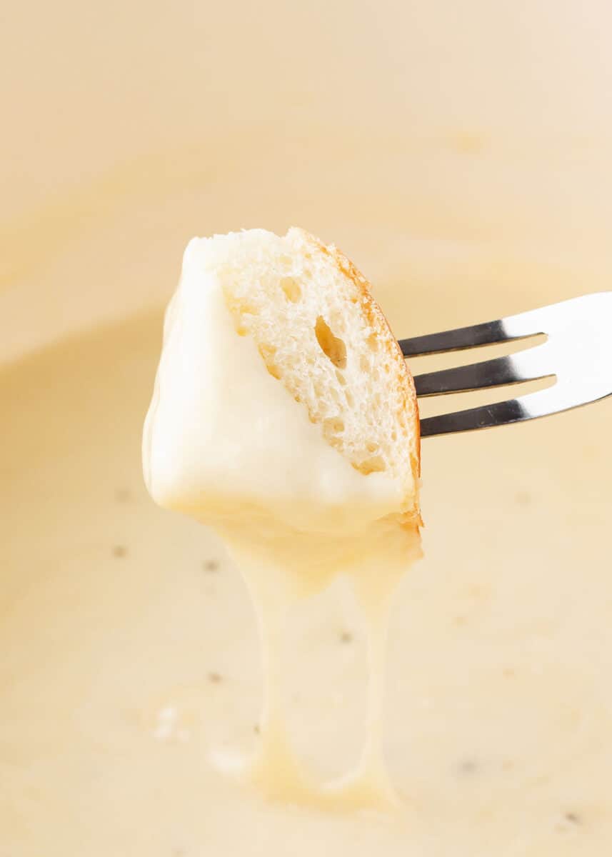 Fork dipping bread into cheese fondue.