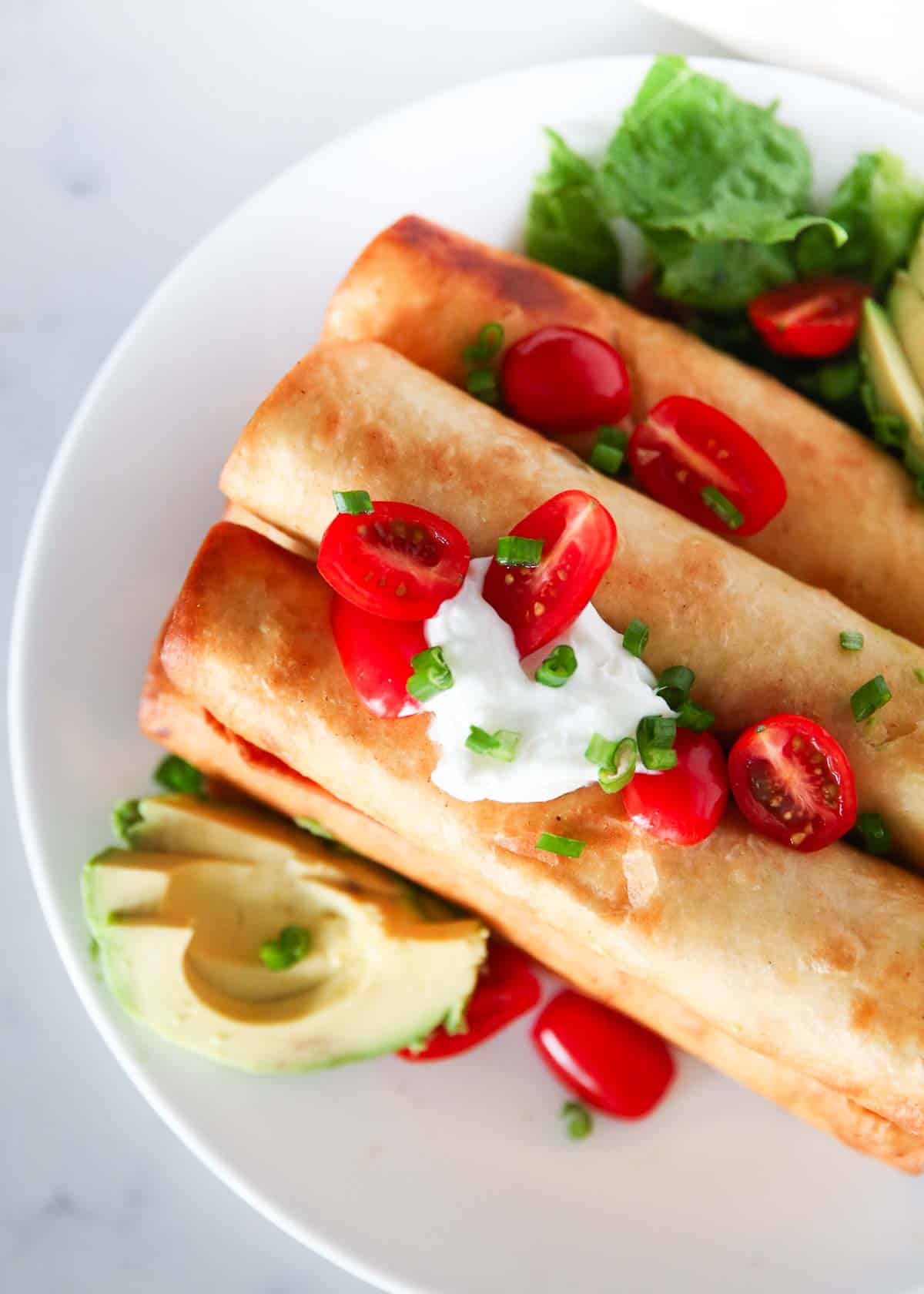 Chicken flautas on a white plate with toppings.