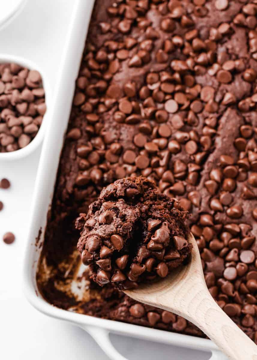 Chocolate dump cake in a white baking dish with wooden spoon.