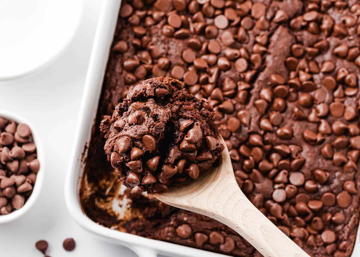 Chocolate dump cake in a white baking dish with a wooden spoon.