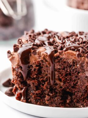 Chocolate poke cake on a white plate with chocolate chips.