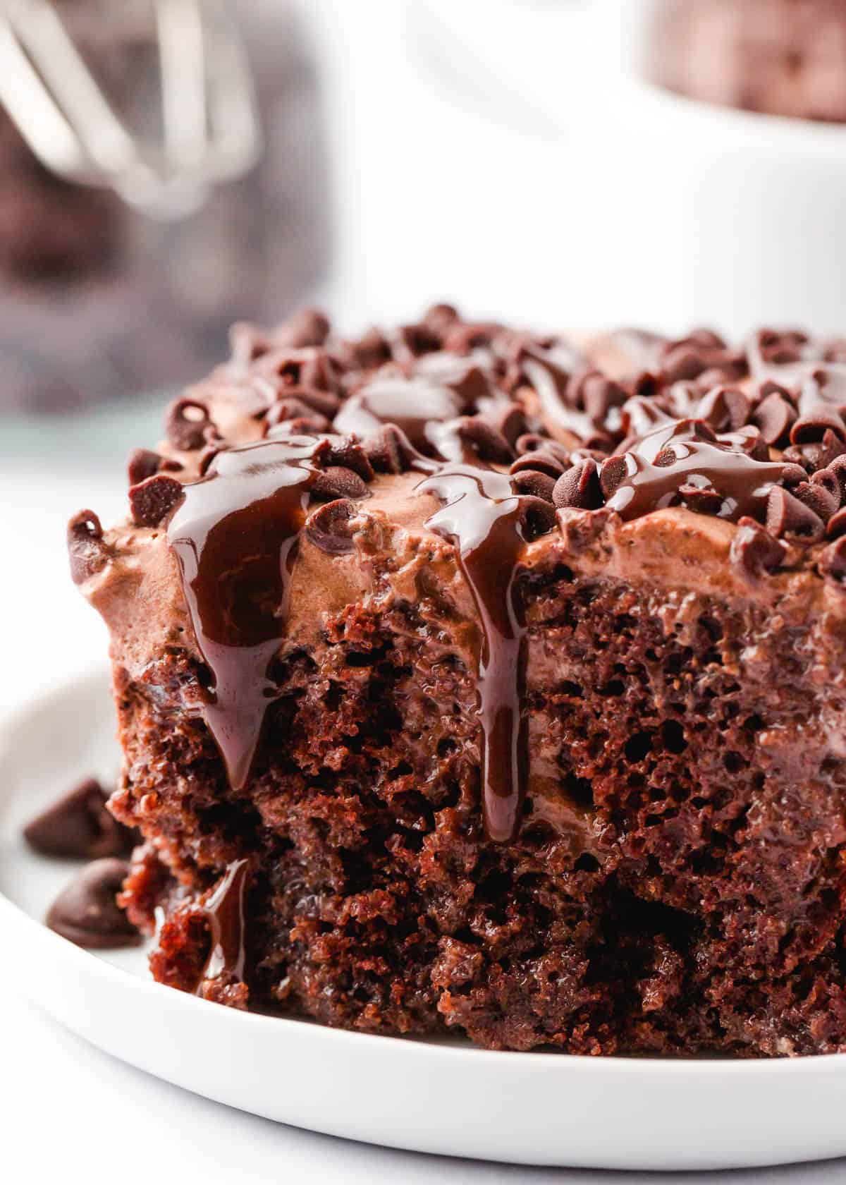 Chocolate poke cake on a white plate with chocolate chips.