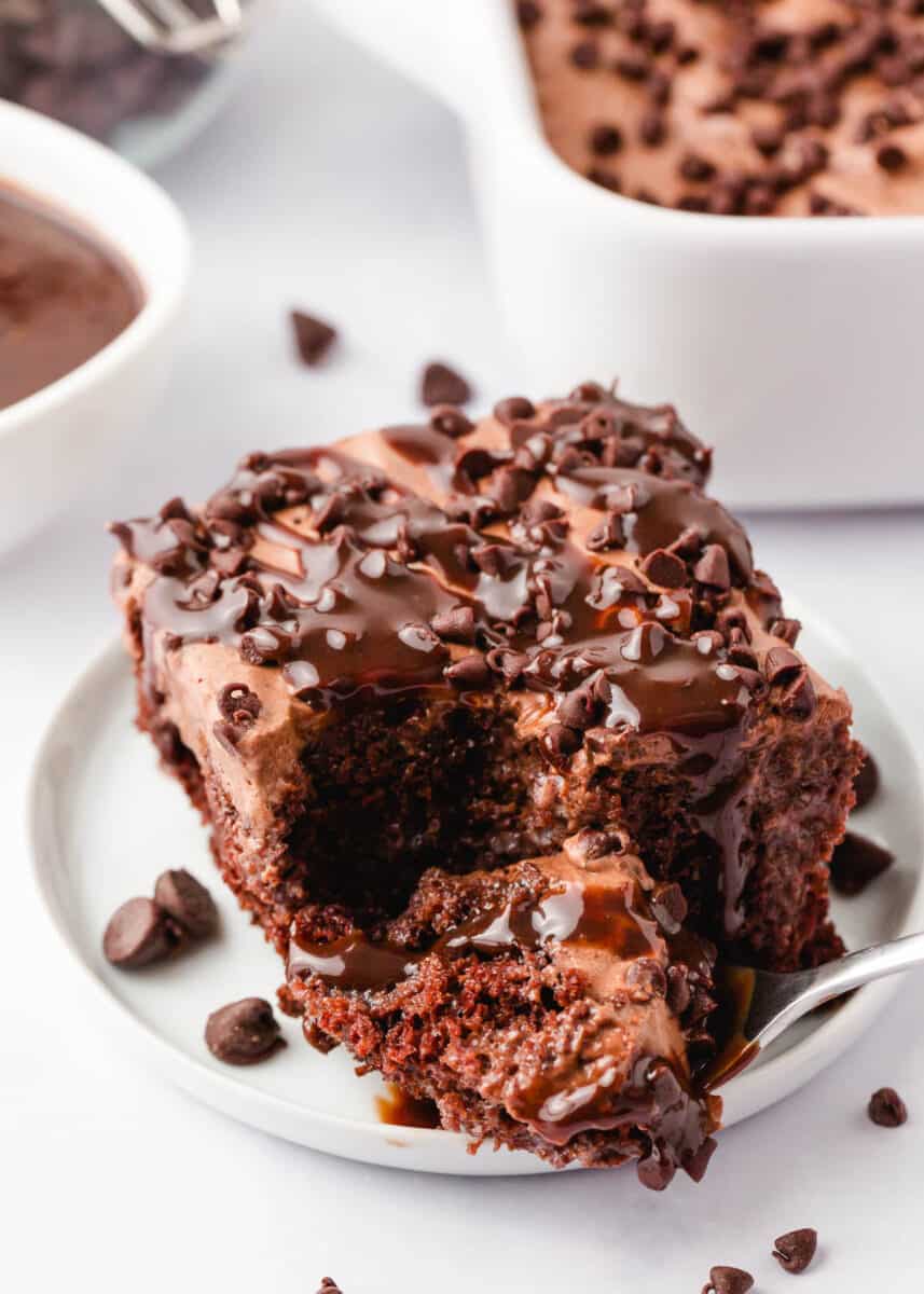 Chocolate poke cake on a white plate with a bite taken.