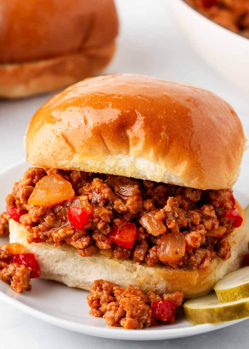 Sloppy Joe with pickles on a white plate.