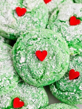 A close-up view of a soft green Grinch cookie coated in powdered sugar with a small red heart in the center.