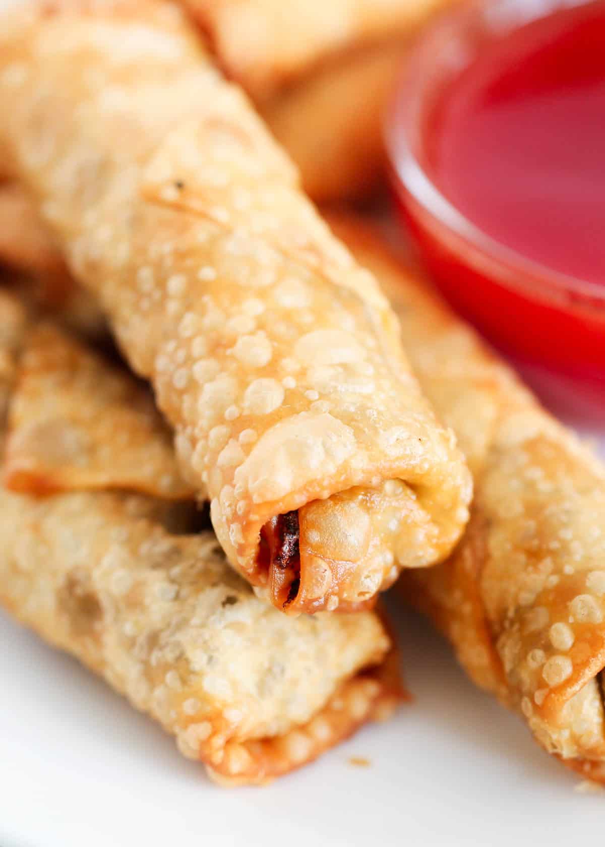 Upclose photo of egg rolls stacked on top of each other with sweet and sour sauce. 