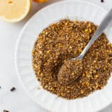 Lemon pepper seasoning in a white bowl with a spoon.