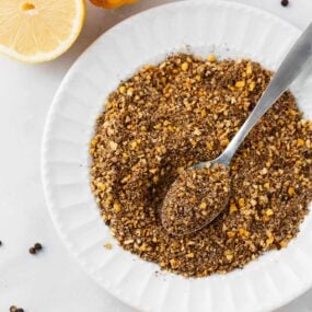 Lemon pepper seasoning in a white bowl with a spoon.