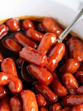 Lil smokies in a white crockpot with a spoon.