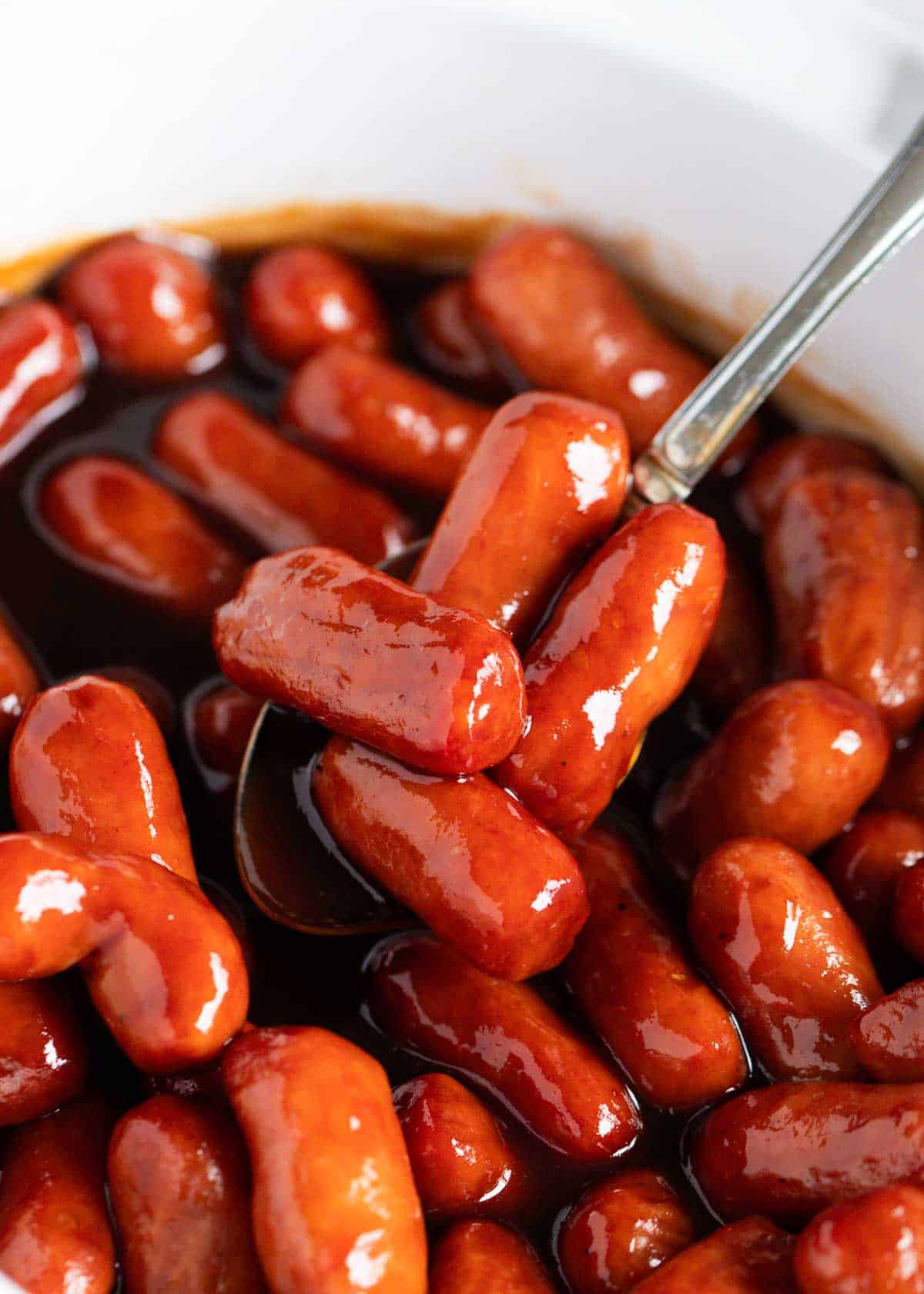 Lil smokies in a white crockpot with a spoon.