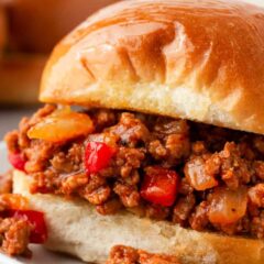 Close-up of a sloppy joe sandwich on a bun with saucy ground beef filling and red peppers.