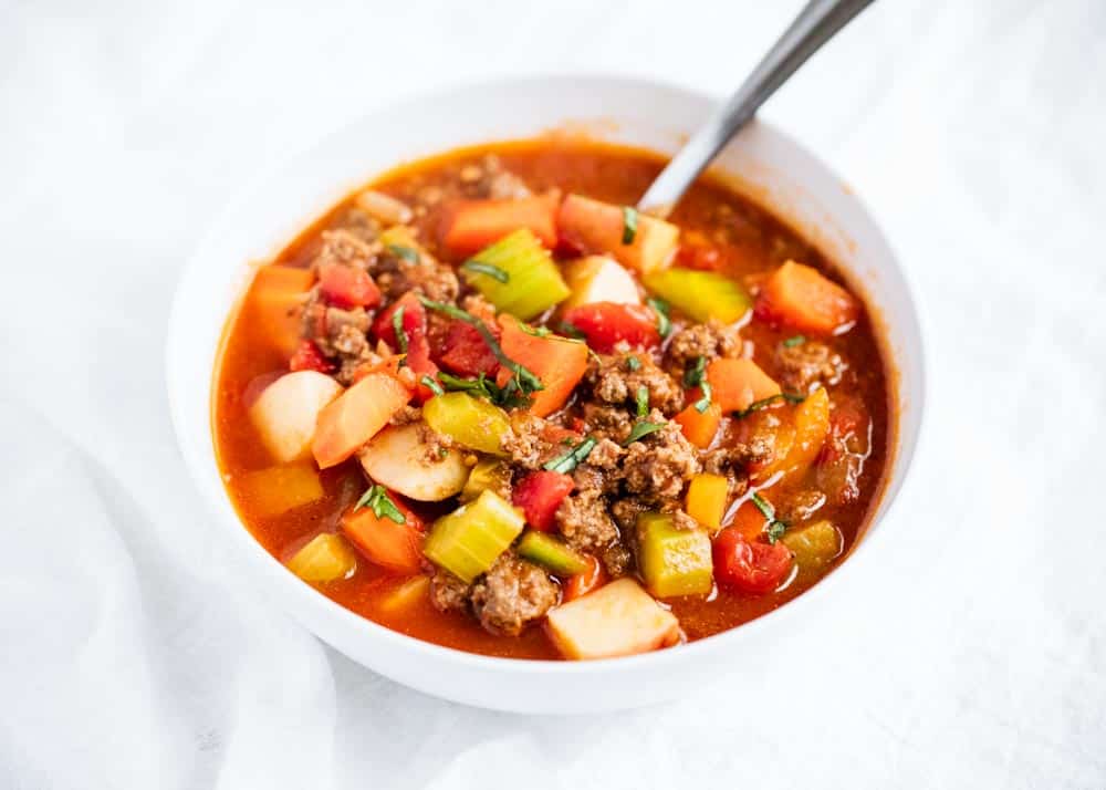 Vegetable beef soup in a white bowl with spoon.