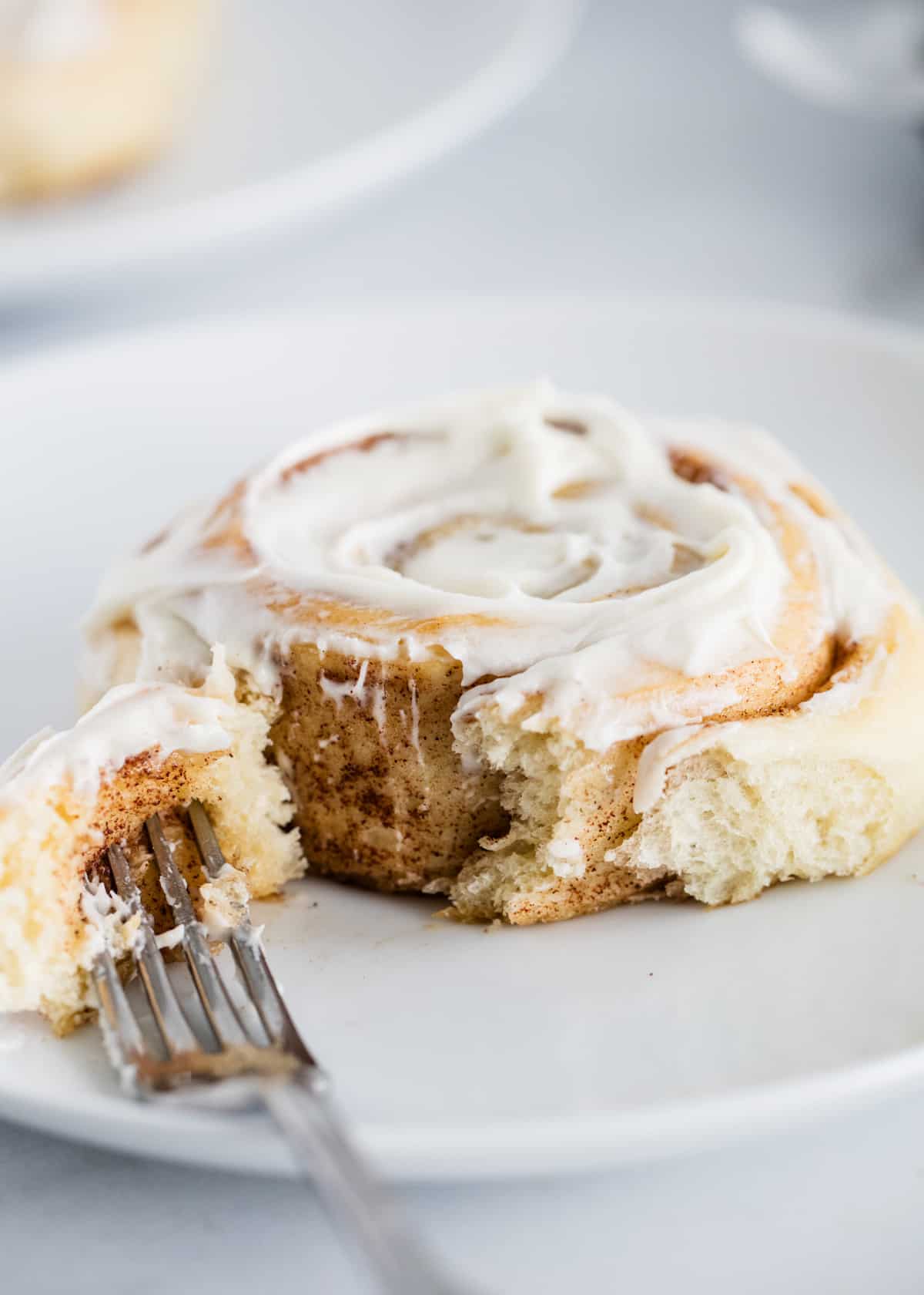Cinnamon roll on a white plate with a fork taking a bite out of it. 