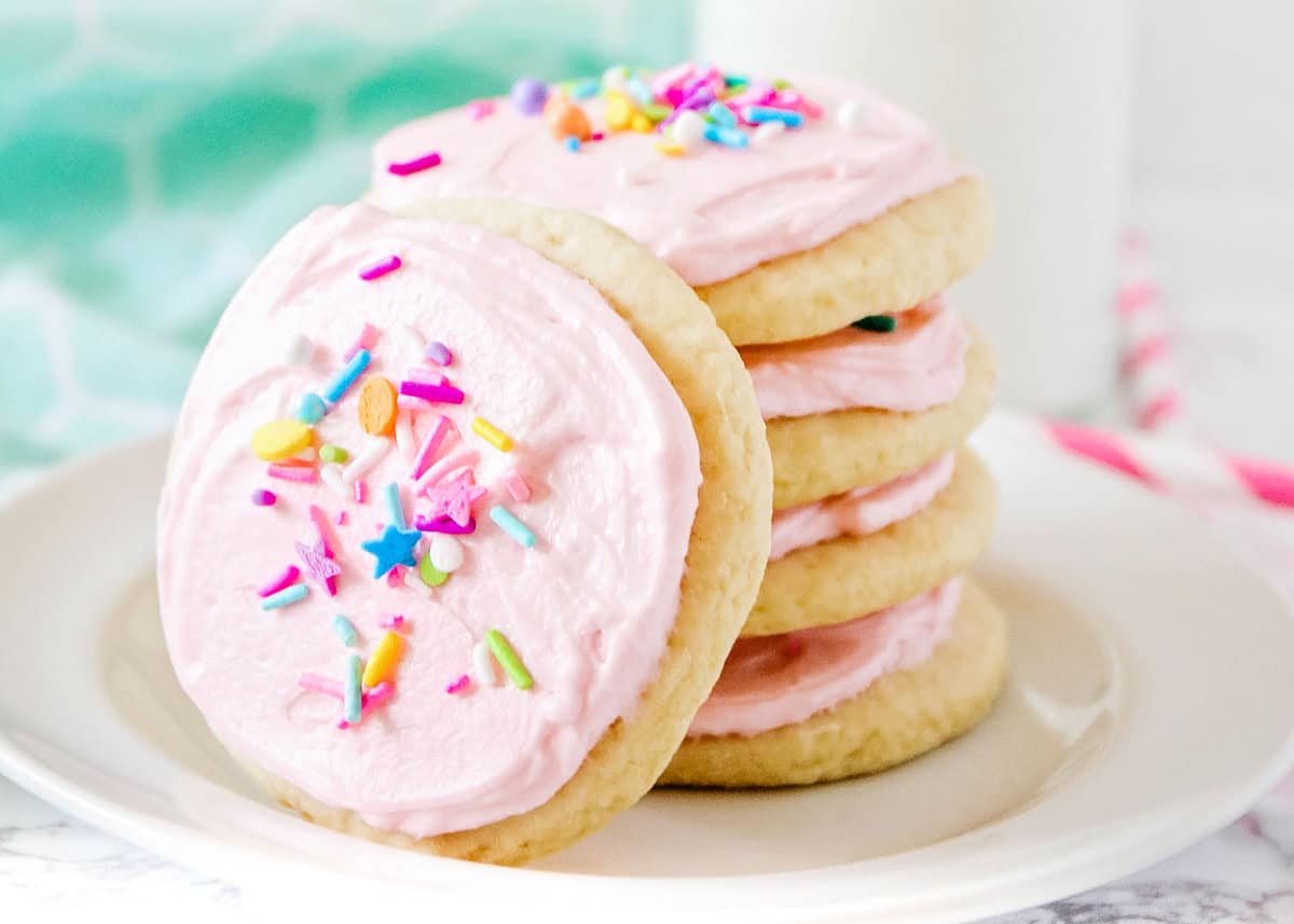 Soft sugar cookies with frosting stacked on a white plate.