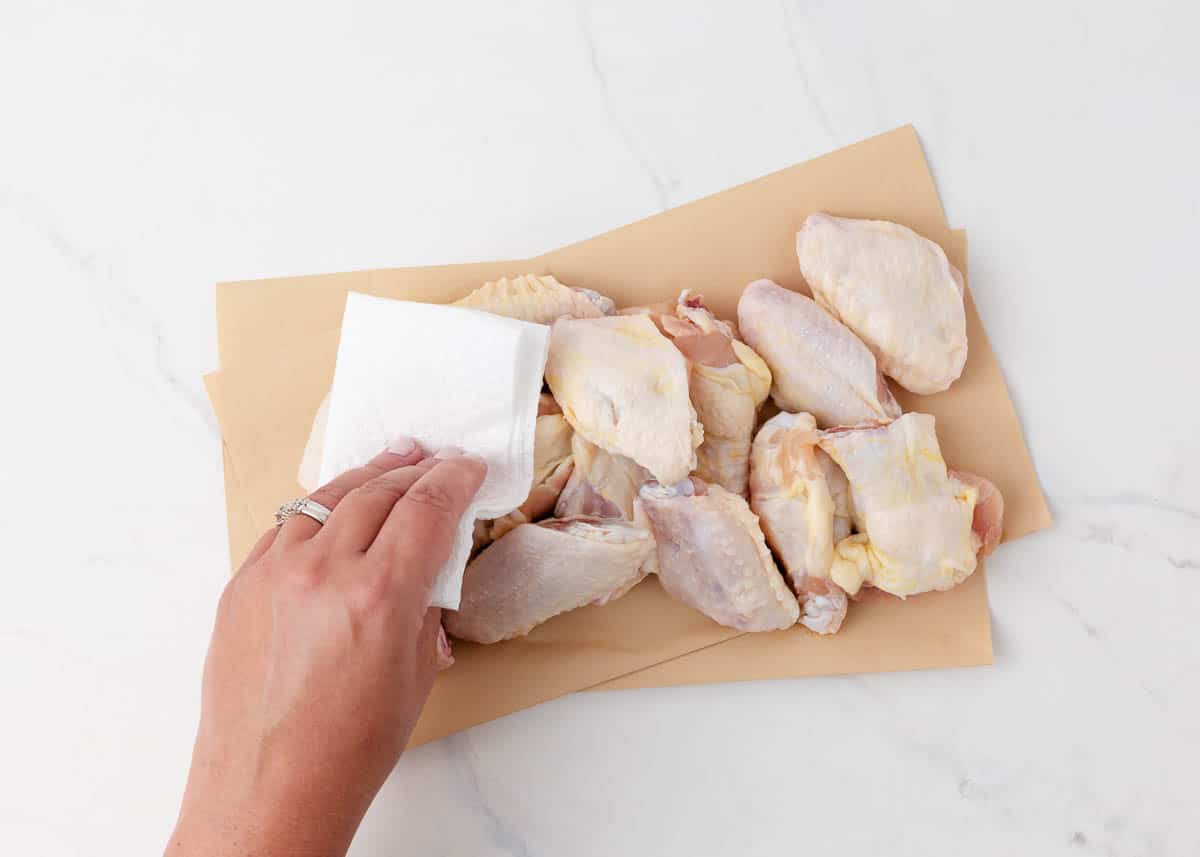 Patting chicken wings with paper towel on the counter.