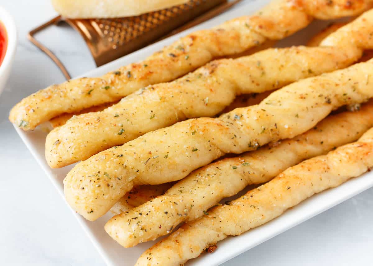Breadsticks stacked on white plate.
