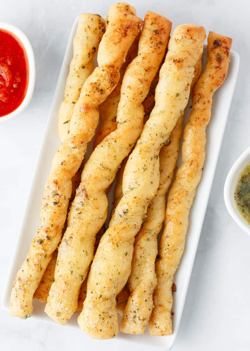 Breadsticks with marinara and pesto on white plate.