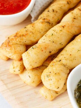 Breadsticks stacked on a wooden board.