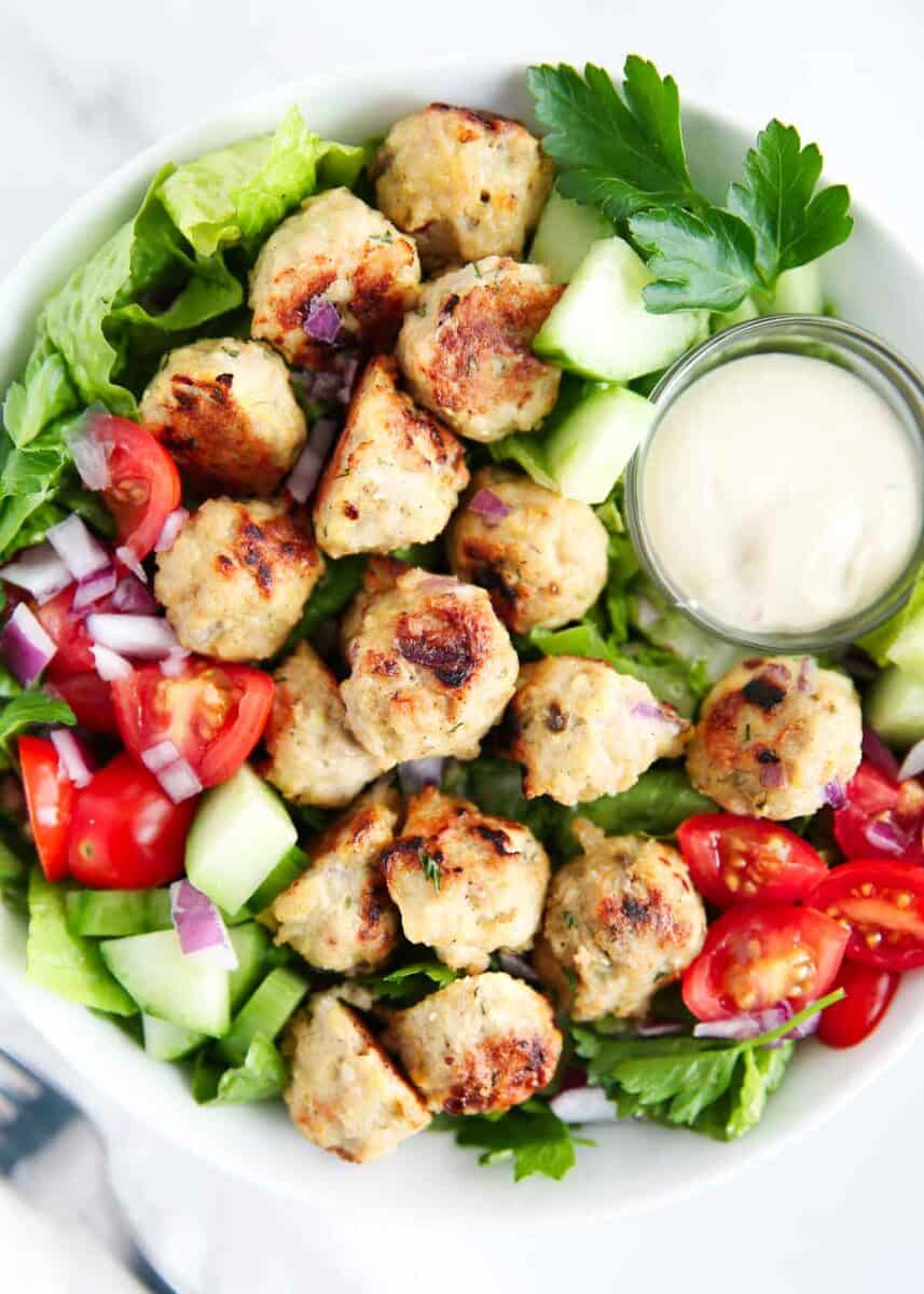 Greek meatballs on top of a salad in a bowl.
