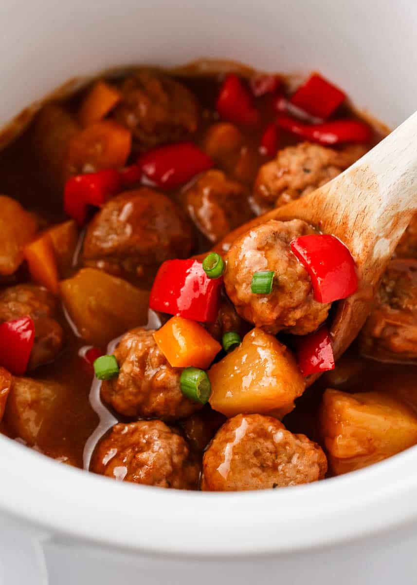 Hawaiian meatballs in a crockpot with a spoon.