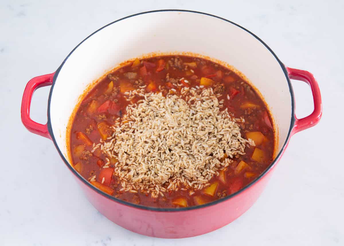 The ingredients to stuffed pepper soup in a red dutch oven pot. 