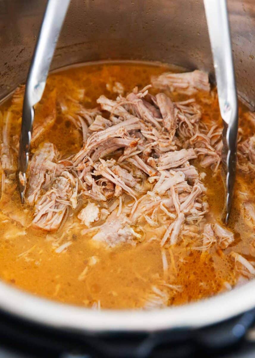 Carnitas cooking in instant pot with tongs. 