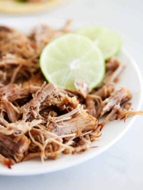 Instant pot carnitas on a white plate with lime.