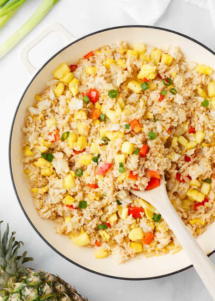 Pineapple fried rice in a white pot with wooden spoon.