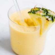 Pineapple smoothie in glass cup with pineapple slice.