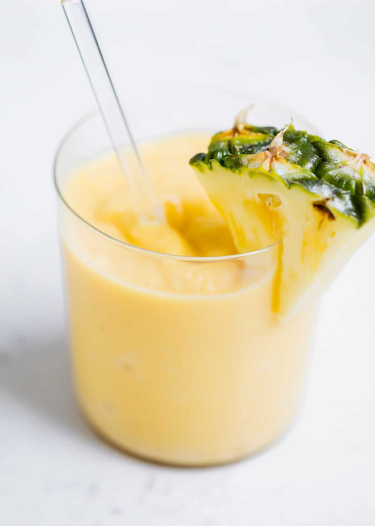 This healthy pineapple smoothie is creamy, refreshing and tastes downright tropical. It's easy to make in only 5 minutes with 5 ingredients and is perfect for breakfast, snack, or anytime you crave something sweet and fruity! Pineapple smoothie in glass cup with pineapple slice.