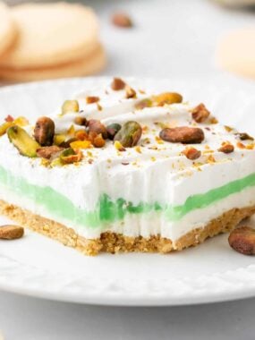 Layered pistachio dessert on plate with a small bite removed to show creamy layers with shortbread crust.