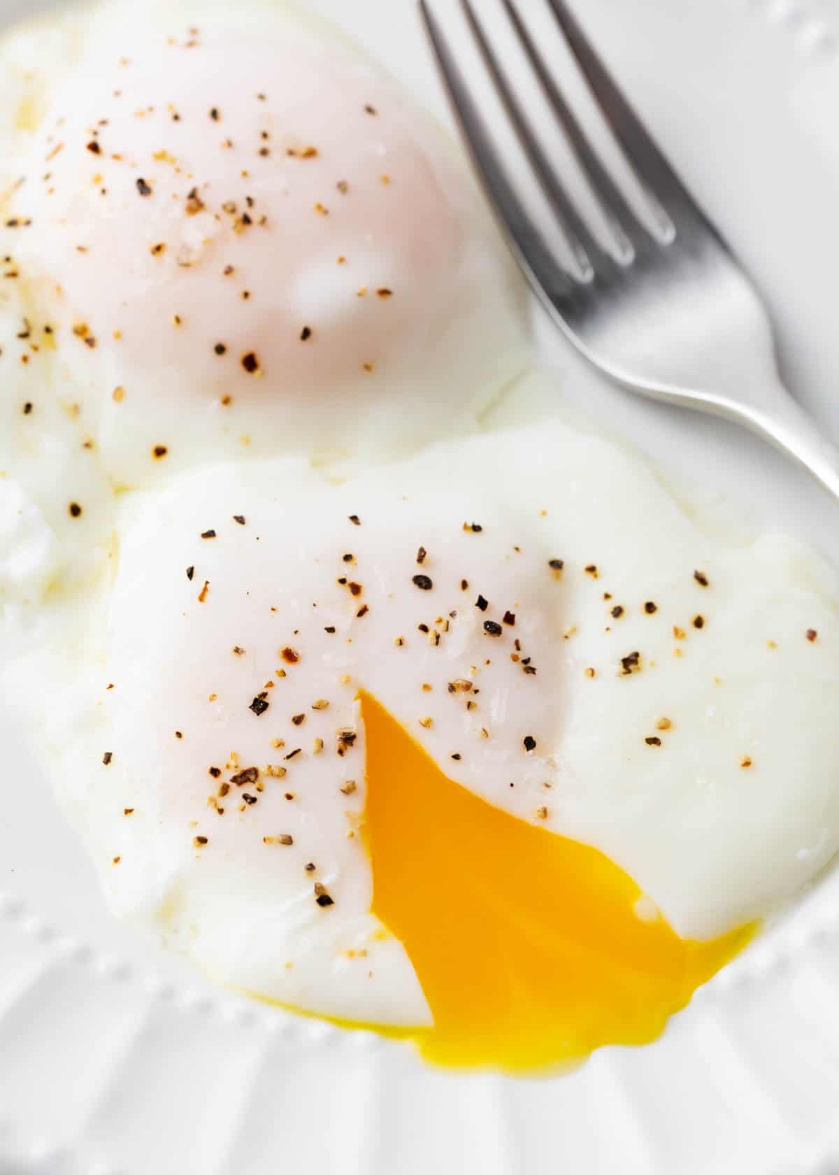 Poached eggs cut open on white plate.