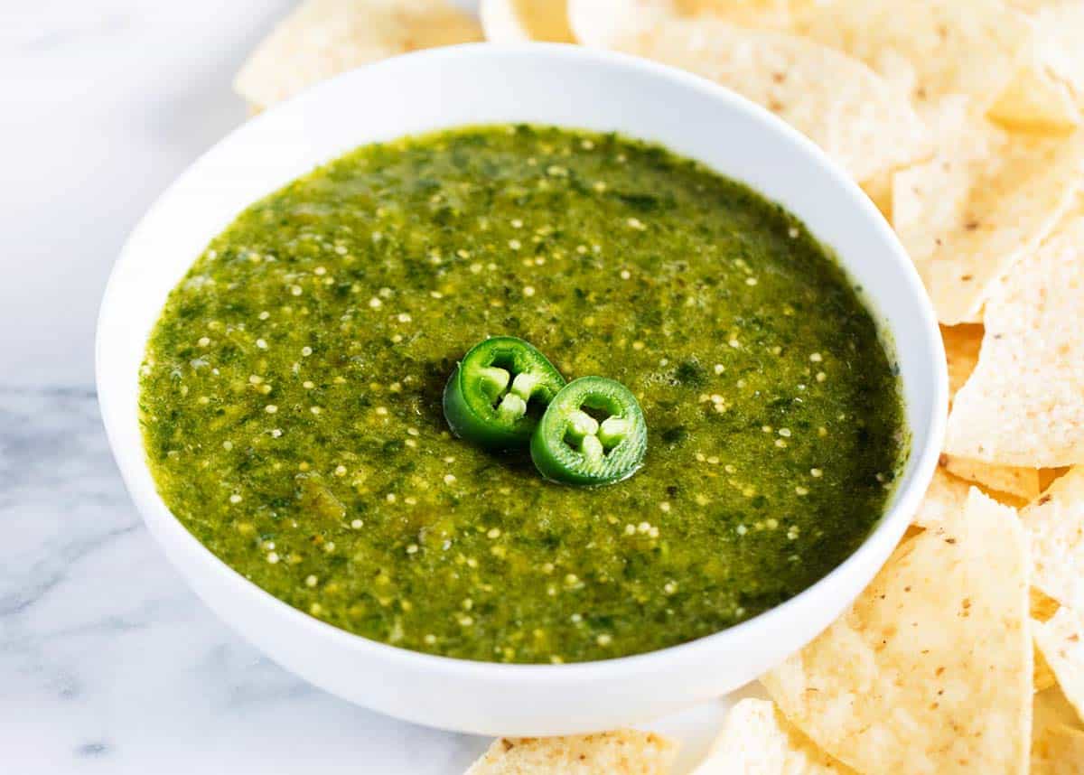 Salsa verde in a white bowl with chips all around. 