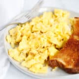 Scrambled eggs on a plate with toast and a fork.