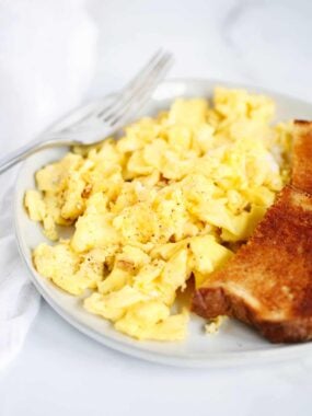 Scrambled eggs on a plate with toast and a fork.