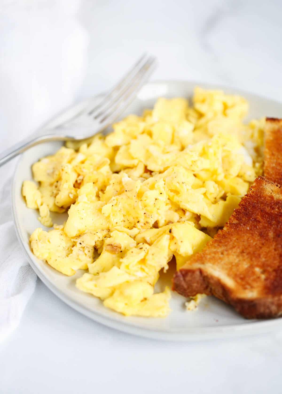 Scrambled eggs on a plate with toast and a fork.