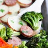 Sheet pan sausage and veggies on a sheet pan with a spoon..