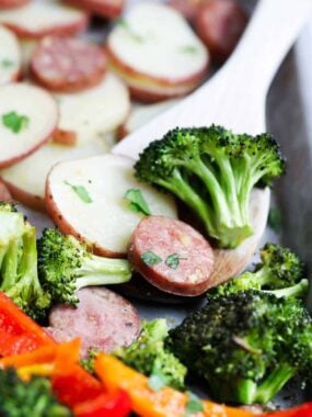Sheet pan sausage and veggies on a sheet pan with a spoon..