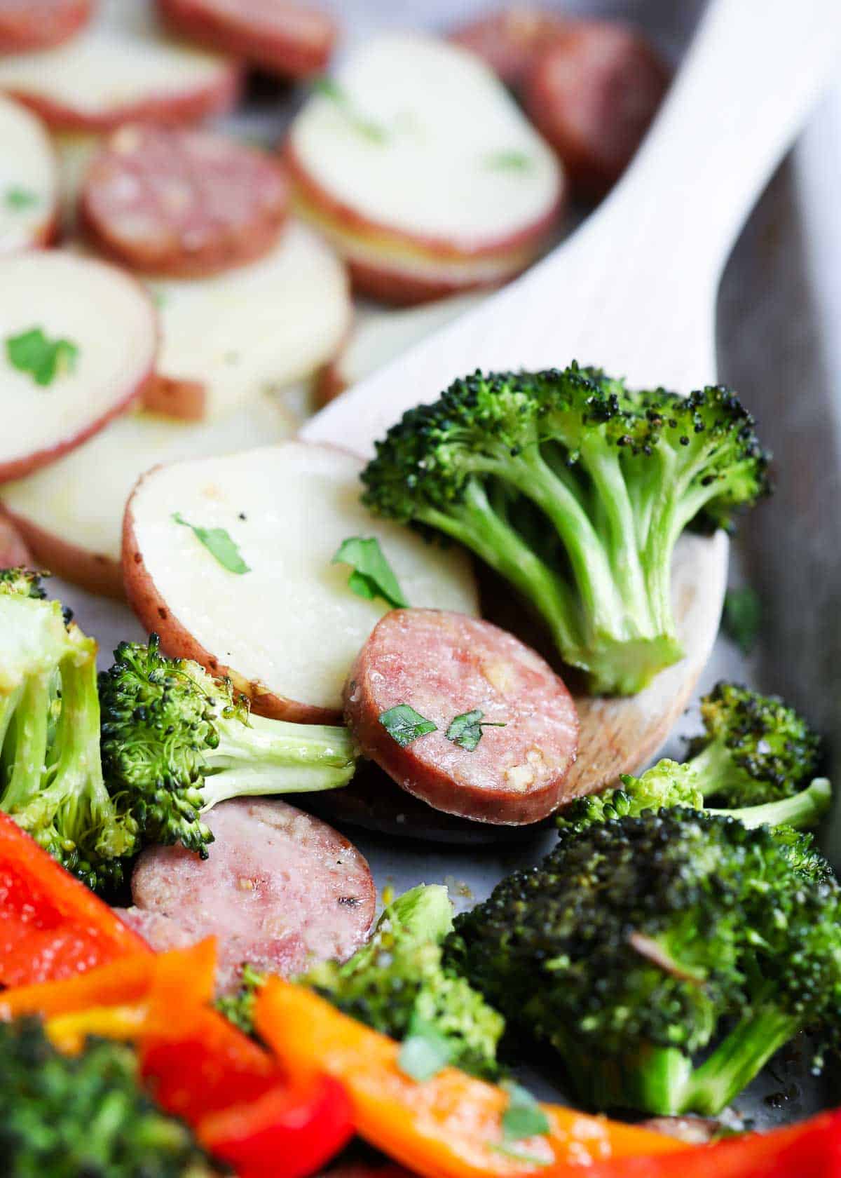 Sheet pan sausage and veggies on a sheet pan with a spoon..