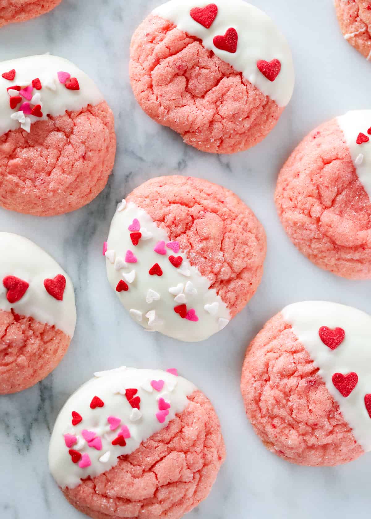 Strawberry cookies dipped in a white frosting with colorful hearts. 