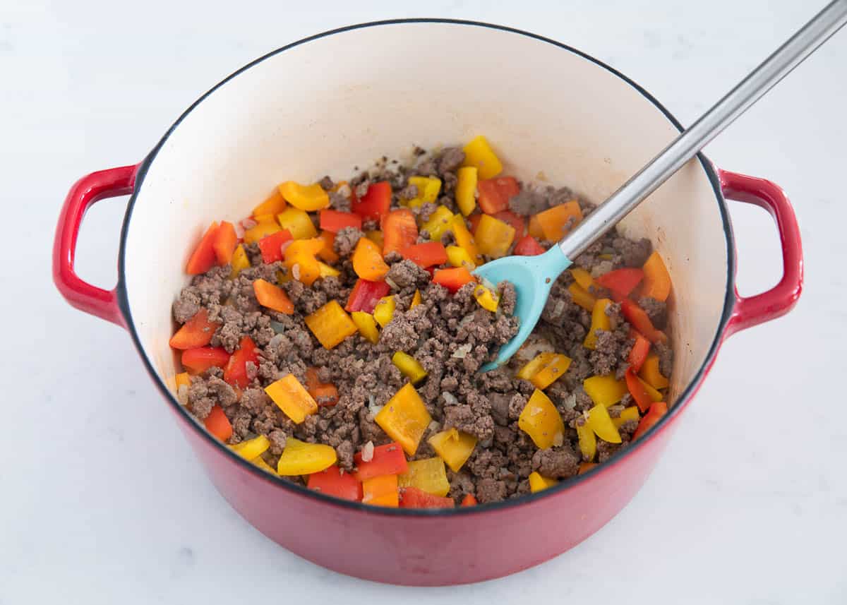 A red pot with bell peppers and ground beef stirred together. 