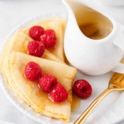Swedish pancakes with raspberries and syrup on a white plate.
