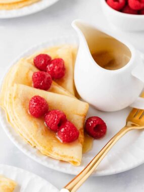 Swedish pancakes with raspberries and syrup on a white plate.