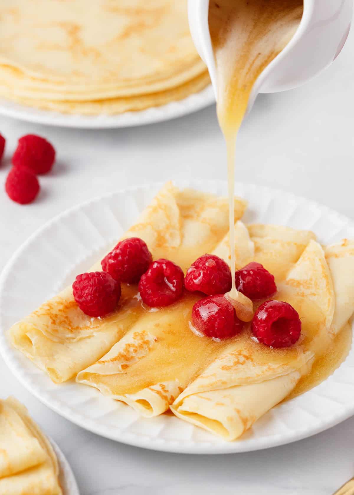 Pouring syrup onto swedish pancakes on a white plate.