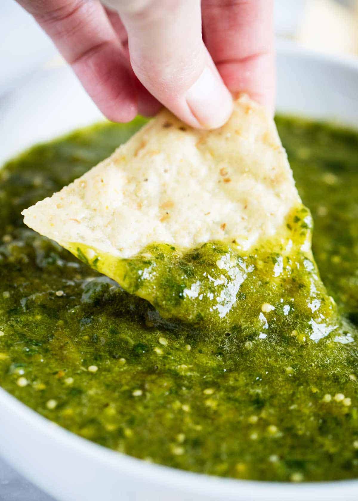 Salsa verde in a bowl with a chip dipped into it.