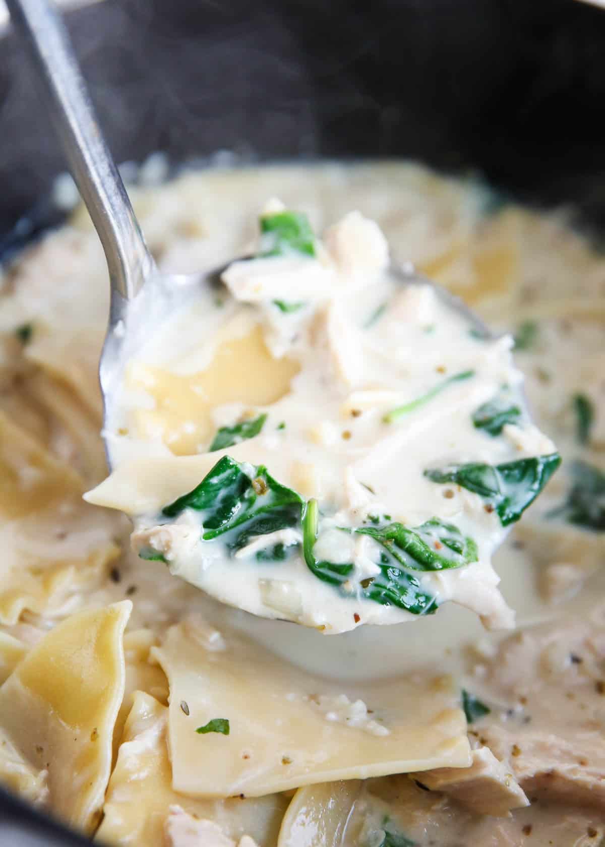 Ladle full of white lasagna soup in a black pot.